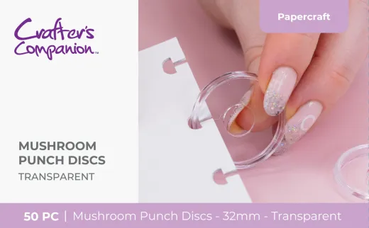 Hand setzt eine transparente Mushroom-Bindescheibe in ein gelochtes weißes Blatt vor rosa Hintergrund ein.
