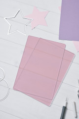 Fliederfarbene Sizzix Cutting Pads auf weißem Holztisch mit Stanzschablonen und Papiersternen