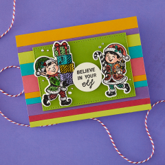 Bunt gestreifte Karte mit zwei kolorierten Elfen - eine trägt Geschenke, die andere ein Kuscheltier - grünem Rahmen und Spruch 'Believe in your elf'.