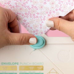 Hände bedienen das turquoise Stanzrad des Mini Punch Boards, Rosa Blumenpapier wird gestanzt