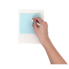 Hand mit weißem Ritzmesser auf türkisem Papier auf dem Ritzbrett