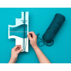 Hände zeigen die Verwendung des Tassel Loom mit dunkelgrünem Garn auf türkisfarbenem Hintergrund