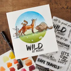 Anwendungsbeispiel: aquarellierte Waldtier-Szene neben Stempeln 'Adventure Awaits', 'Safe Travels' und Aquarellfarben.
