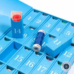 Geöffnete Fächer des Aurifil Adventskalenders mit zwei entnommenen Garnspulen in Blau und Rot