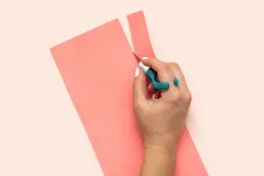 Hand schneidet rosa Bastelkarton mit We R Comfort Craft Messer, ergonomische Fingerposition