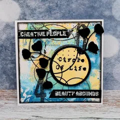 Blau-gelbe Karte mit Kreis-Stempelmotiv, Knospenzweig-Stanzform und Wortstickern „Circle of Life", „Creative People", „Beauty Abounds"