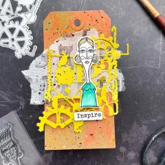 Gelb foliierte Zahnrad-Stanzform auf orange-rosa Karte mit gestempelter Mädchenfigur und Wortsticker „Inspire"