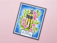 Kolorierte Grußkarte mit Laterne, rosa Blüten und dem Schriftzug 'Happy Anniversary'.
