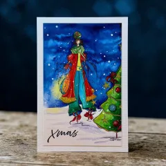 Karte mit der Figur im rot-grünen Mantel und Laterne vor nächtlichem Sternenhimmel, auf Holztisch fotografiert.