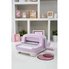 Sizzix Big Shot Lilac auf Schreibtisch mit weißem Regal, daneben Bastelarbeiten und Schneidepads