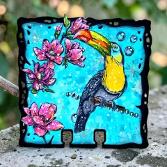 Quadratische Karte in leuchtendem Blau mit Tukan und rosa Blüten