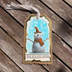 Koloriertes Anhänger-Tag mit gestempeltem Cheery Snowman Motiv vor hellblauem Hintergrund.