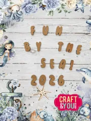 Aus Kraftpapier-Chipboard gestanzte Buchstaben und Zahlen als Schriftzug "Fun by the Sea! 2026" auf Holzoptik-Hintergrund mit Meerjungfrau, Delfin und Oktopus
