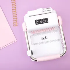 Cinch Bindewerkzeug neben spiral-gebundenem Notizbuch mit floralen Motiven auf Rosa
