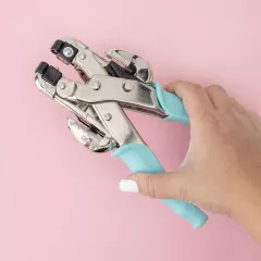 Hand hält geöffneten Crop-A-Dile Stanzer mit türkisem Griff in Aktion vor rosa Hintergrund