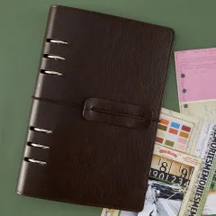 Geschlossenes dunkelbraunes Ringbuch auf grünem Hintergrund neben Vintage-Ephemera und Farbmusterkarte