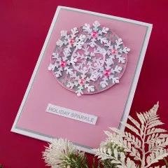 Detailaufnahme des Schneeflockenkranzes mit Strasssteinen und rosa Perlen auf gestreiftem Karton.