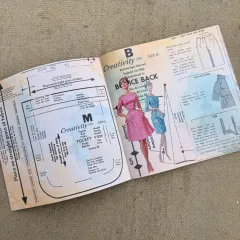 Aufgeschlagene Doppelseite mit Schnittmusterbogen sowie zwei aufgemalten Modefiguren in rosa und türkisem Kleid.