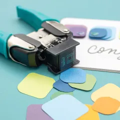 Gefertigte abgerundete Papierstücke aus verschiedenen Farben neben Corner Chomper Tool, Bastelresultate sichtbar