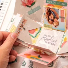 Geöffnete bunte Explosionsbox mit Fotos, Texten, Washi-Tape und Deko-Details in Rosa, Grün und Gelb