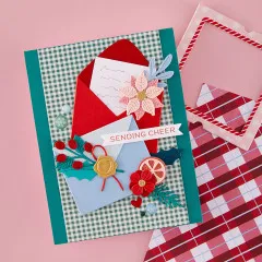 Fertige Weihnachtskarte mit rotem Mini-Umschlag, Weihnachtsstern-Applikation und dem Spruch 'Sending Cheer' auf kariertem Karton.