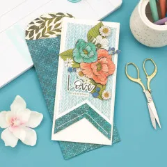 Rosa gestaltete Slimline-Karte mit dekorativen Elementen neben Punch Board und Stiften auf blauem Hintergrund