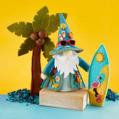 Fertig genähtes 3D-Filzprojekt: Sommer-Gnom mit spitzem Hut, Sonnenbrille, weißem Bart und gemustertem Umhang neben Filz-Palme und Surfboard mit Flamingo-Motiv auf blauem Untergrund