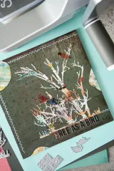 Karte mit Baum aus Collagepapier auf dunkelgrünem Grund, roten Vögeln und Free as a Bird, daneben die Stanzen