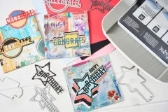 Übersicht aus Stanzformen, gestalteten Karten und Cardstock neben der Sizzix Stanzmaschine