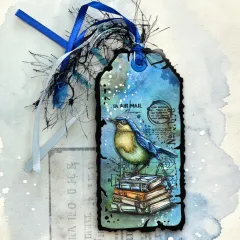Geschenkanhänger mit Vogel-Stempel auf gestapelten Büchern und blauem Band