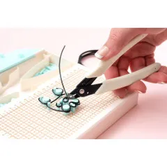 Schachtel Happy Jig in Hand mit Design-Vorlage und schwarzem Draht-Anhänger, Anleitung im Hintergrund