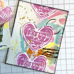 Mixed-Media-Seite mit pinkfarben gestempelten Herzen, Farbflächen und Spritzern