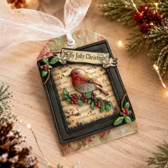 Gegossener und bemalter Rotkehlchen-Anhänger auf Buchseiten-Hintergrund mit Banderole „Holly Jolly Christmas" und Holly-Eckverzierung