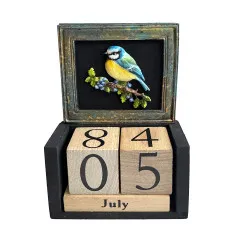 Ewiger Holzblock-Kalender mit gegossenem, blau-gelb bemaltem Vogel in dunklem Rahmen über den Datumswürfeln