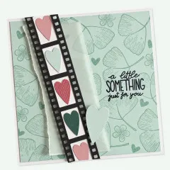 Mintgrüne Karte mit schwarzem Filmstreifen, Herzen in Rosa und Grün und Spruch a little something just for you