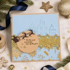 Hellblaue Weihnachtskarte mit geprägten Häusern, Rentierschlitten und goldenem Sternenband