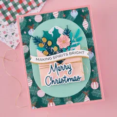Rosa Weihnachtskarte mit grünem Christbaumschmuck-Muster, gestanztem Umschlag mit Blumen und goldener Kordel, Banner 'Making Spirits Bright' und Schriftzug 'Merry Christmas'.