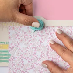 Detailaufnahme: Hände positionieren bedrucktes Blumenpapier unter türkisem Stanzrad des Mini Punch Boards