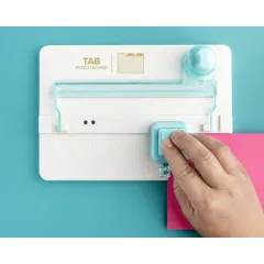 Nahaufnahme Hand beim Lochen mit dem Tab Punch Board, rosa Papierstreifen wird eingefügt