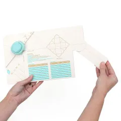 Zwei Hände halten geöffnetes WRMK Gift Box Punch Board mit Maßtabellen und Anleitung