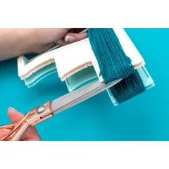 Schere schneidet dunkelgrünes Garn am unteren Ende des Tassel Looms durch, um Quasten zu formen
