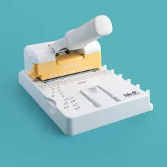 Multi-Cinch Stanzmaschine mit eingesetzter gelber Spiral Stanzkassette bei der Verwendung auf Papier
