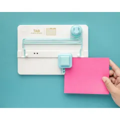 Hand hält rosa Papier bei Punch-Vorgang am Tab Punch Board, Türkis-Blauer Hintergrund