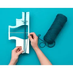 Hände zeigen die Verwendung des Tassel Loom mit dunkelgrünem Garn auf türkisfarbenem Hintergrund