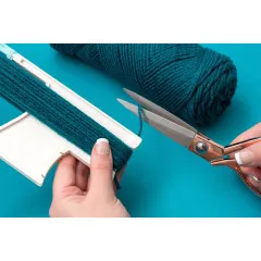 Schere und Tassel Loom mit bewickeltem dunkelgrünem Garn und Garnrolle auf Türkis