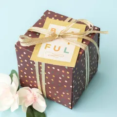 Fertige Geschenkbox aus braun gepunktetem Papier mit goldenem Band und Etikette auf hellblauem Hintergrund