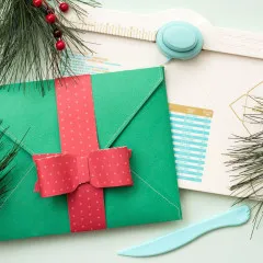 Grüner und roter Umschlag mit roten Punkten, Schleife und Kiefer-Zweige neben Punch Board zur Weihnachtszeit