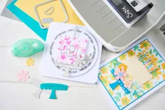 Übersicht aus Stanzformen, Cardstock und fertigen Kuchen-Grußkarten neben der Stanzmaschine