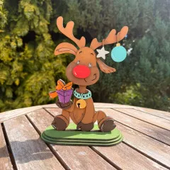 Bemaltes Beispiel der Woodology Reindeer Figur mit roter Nase und bunten Ohrringen im Freien.